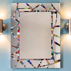 Peut inclure: Un miroir mural rectangulaire doté d'une bordure décorative composée de nombreuses petites tuiles de verre multicolores disposées en un motif mosaïque géométrique fragmenté. La surface réfléchissante centrale est claire et entourée de ces pièces.
