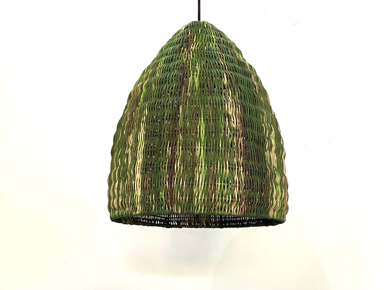 May include: A dome-shaped pendant light made of woven wicker in shades of green, beige, and brown. The texture is intricate and the weave creates a unique pattern. The light fixture is ideal for adding a natural and bohemian touch to any space.  The pendant light is shown hanging against a white background.