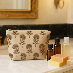 May include: A beige cosmetic bag with a floral pattern, next to several brown glass bottles, a clear bottle, and two bars of soap. The bag has a gold zipper and is sitting on a marble countertop.
