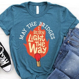 May include: A teal blue t-shirt with a graphic of a matchstick with a flame that says "May the bridges I burn light the way".