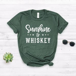 May include: A green t-shirt with the text "Sunshine & WHISKEY" in white lettering. The text is surrounded by four white stars on each side of the ampersand.