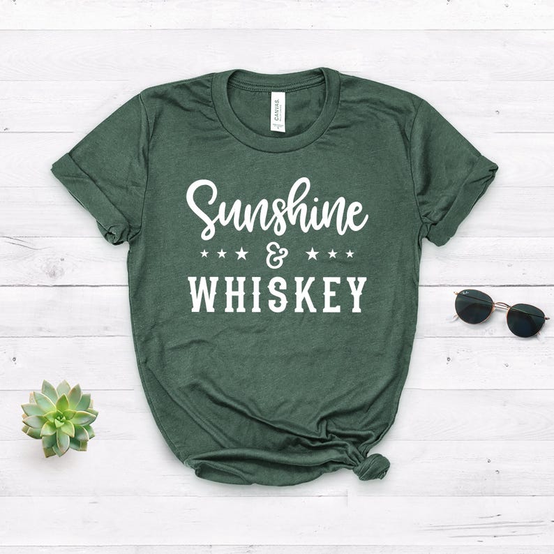 May include: A green t-shirt with the text "Sunshine & WHISKEY" in white lettering. The text is surrounded by four white stars on each side of the ampersand.