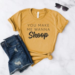 May include: A mustard yellow t-shirt with the text "You make me wanna Shoop" printed in black.