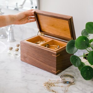 Handcrafted walnut and cherry keepsake box displayed on a marble vanity, used for storing jewelry and keepsakes, with removable compartments and elegant corner spline joinery.