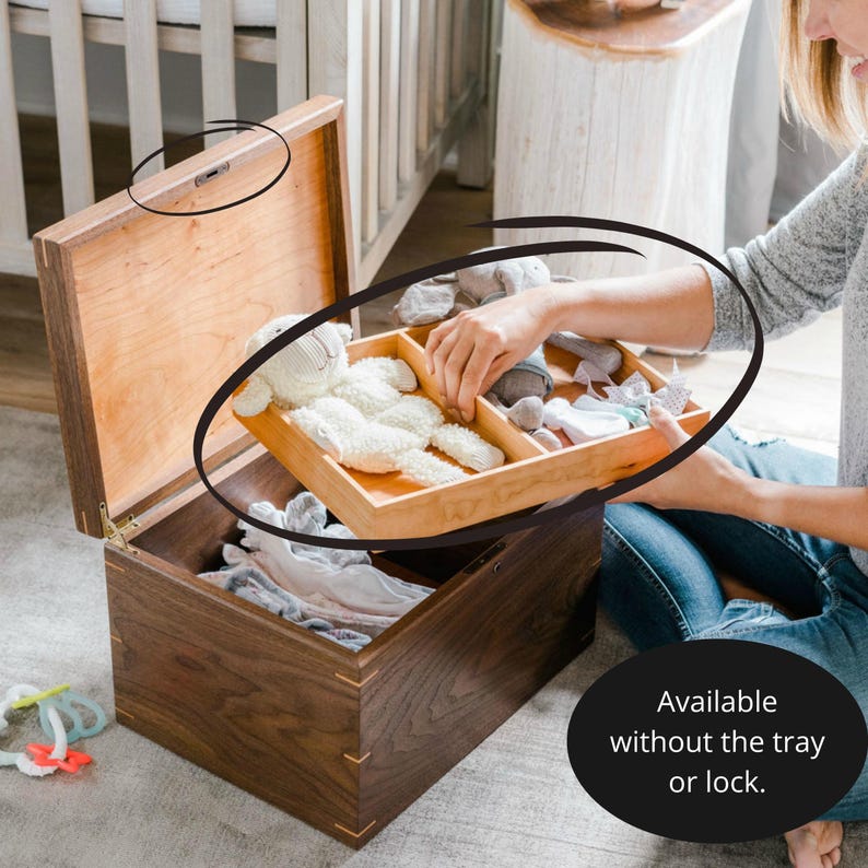 Woman lifting removable tray filled with baby items from an open walnut keepsake box with lock, shown in a nursery setting