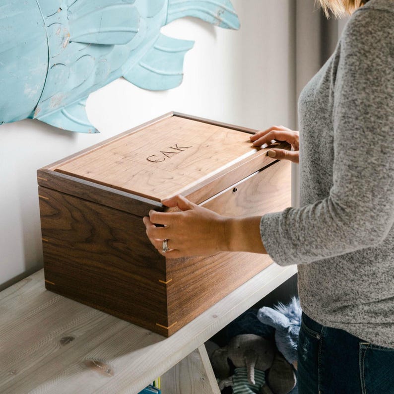 Woman opening personalized walnut keepsake box with engraved initials CAK on a cherry lid, displayed on nursery shelf