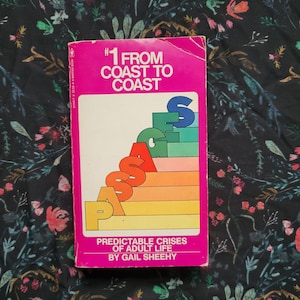 May include: A pink paperback book titled "#1 From Coast to Coast Passages Predictable Crises of Adult Life by Gail Sheehy". The cover features a rainbow-colored staircase with the word "PASSAGES" spelled out in large letters.