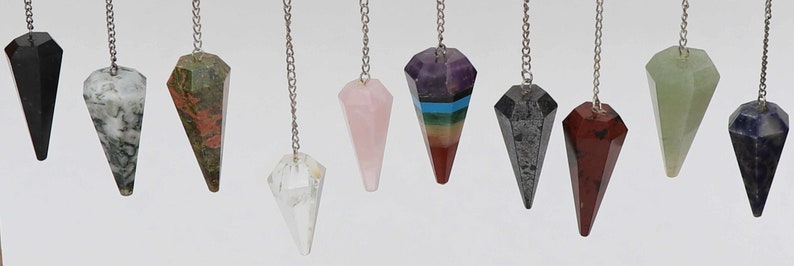 May include: A set of 10 crystal pendulums, each with a different color and shape. The pendulums are made of various crystals, including black obsidian, white agate, green aventurine, pink rose quartz, amethyst, clear quartz, black hematite, red jasper, green jade, and blue lapis lazuli.
