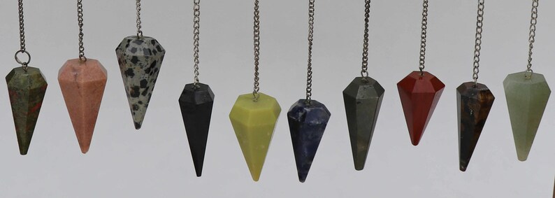 May include: A set of 10 crystal pendulums with silver chains. The pendulums are made of various types of crystals, including green, red, black, and blue.