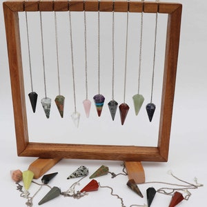 May include: A wooden display stand with 14 crystal pendulums hanging from it. The pendulums are made of various types of crystals, including amethyst, rose quartz, and clear quartz. The stand is on a white surface.