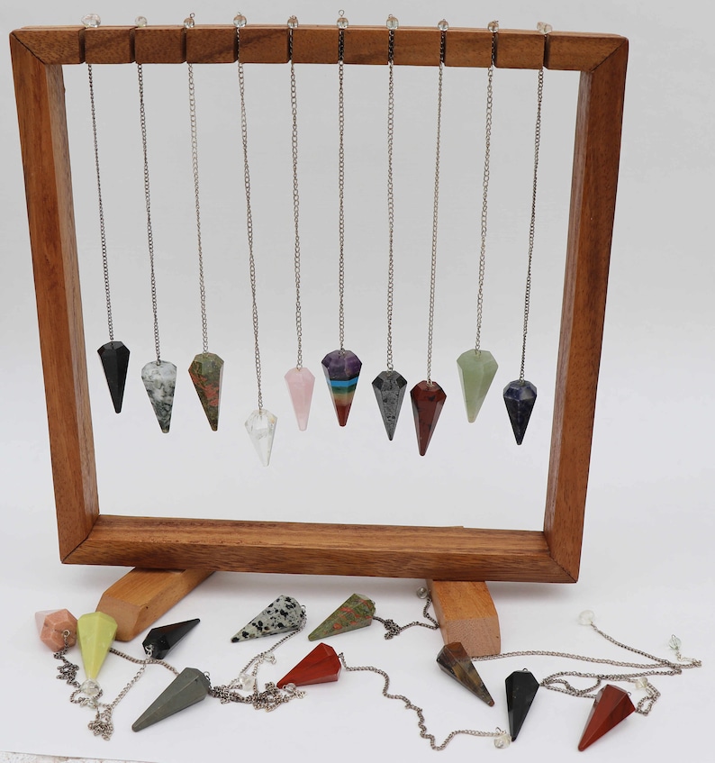 May include: A wooden display stand with 14 crystal pendulums hanging from it. The pendulums are made of various types of crystals, including amethyst, rose quartz, and clear quartz. The stand is on a white surface.