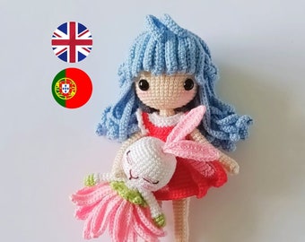 May include: A crocheted doll with blue hair and a red dress holds a crocheted bunny wearing a pink dress.