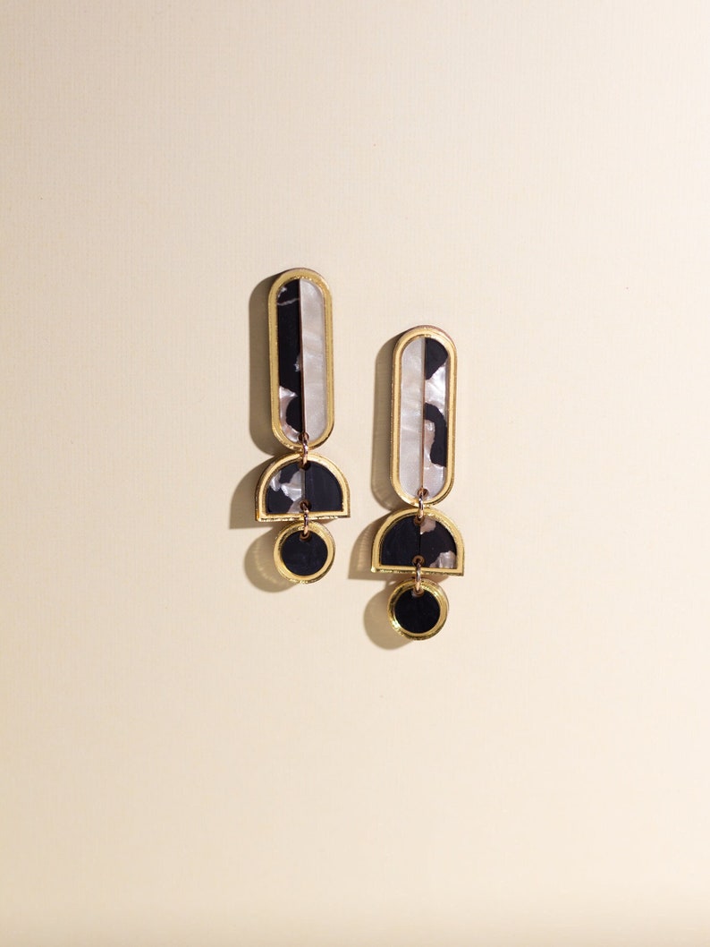 A pair of black, white and gold acrylic statement dangle earrings.