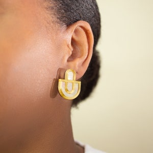 A close up of a model wearing a pair of Mother of Pearl and acrylic statement stud earrings