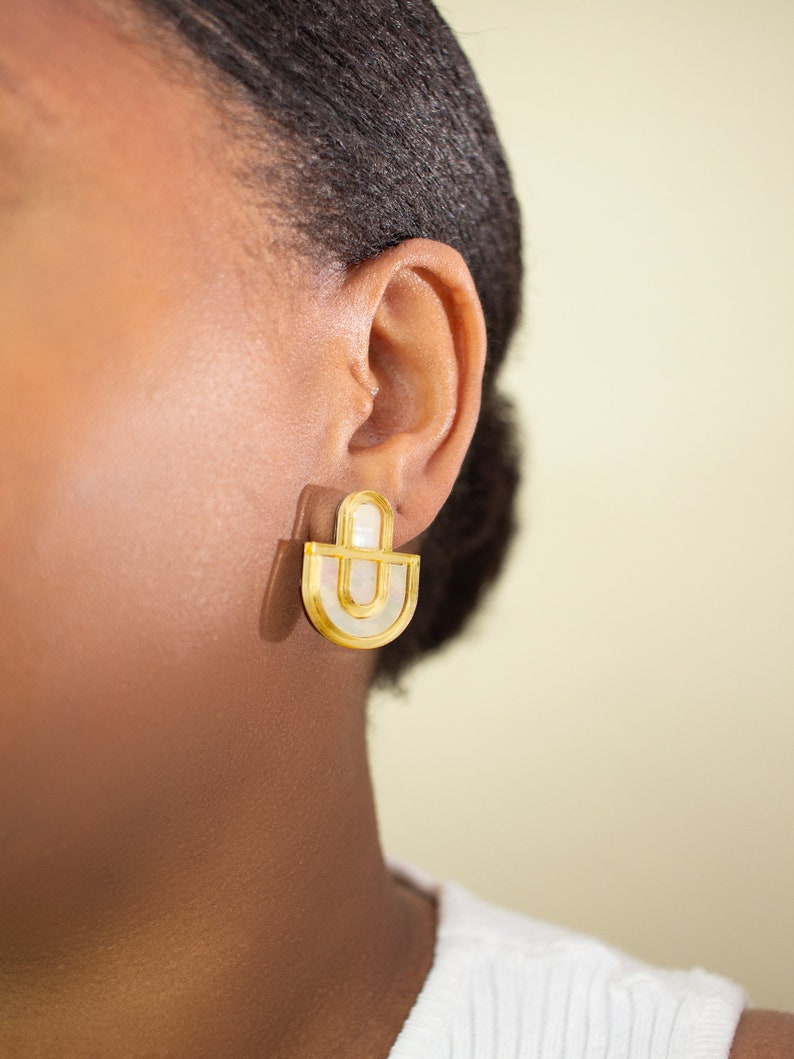 A close up of a model wearing a pair of Mother of Pearl and acrylic statement stud earrings