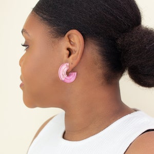 A model wearing a pair of pink acrylic statement hoop earrings.