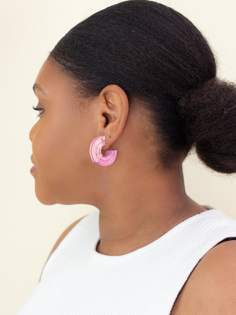 A model wearing a pair of pink acrylic statement hoop earrings.