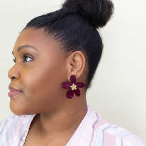 A model wearing a pair of plum purple acrylic statement flower earrings in the size Large