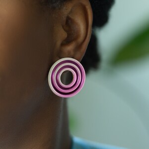 A close up of a model wearing  pink circular multicolored statement stud earrings.