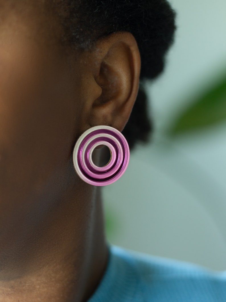 A close up of a model wearing  pink circular multicolored statement stud earrings.