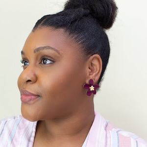 A model wearing a pair of plum purple acrylic statement flower earrings in the size small.