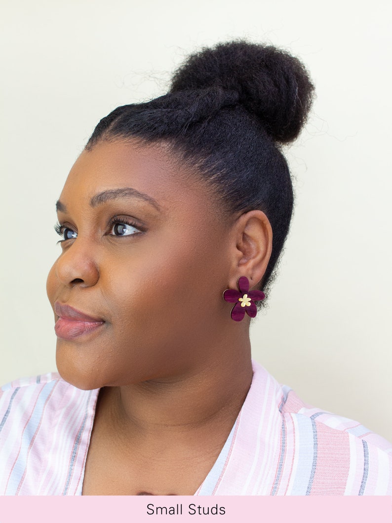 A model wearing a pair of plum purple acrylic statement flower earrings in the size small.