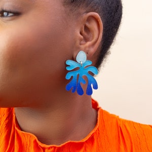 A close up of a model wearing A model wearing a pair of ombre blue Matisse inspired statement dangle earrings.