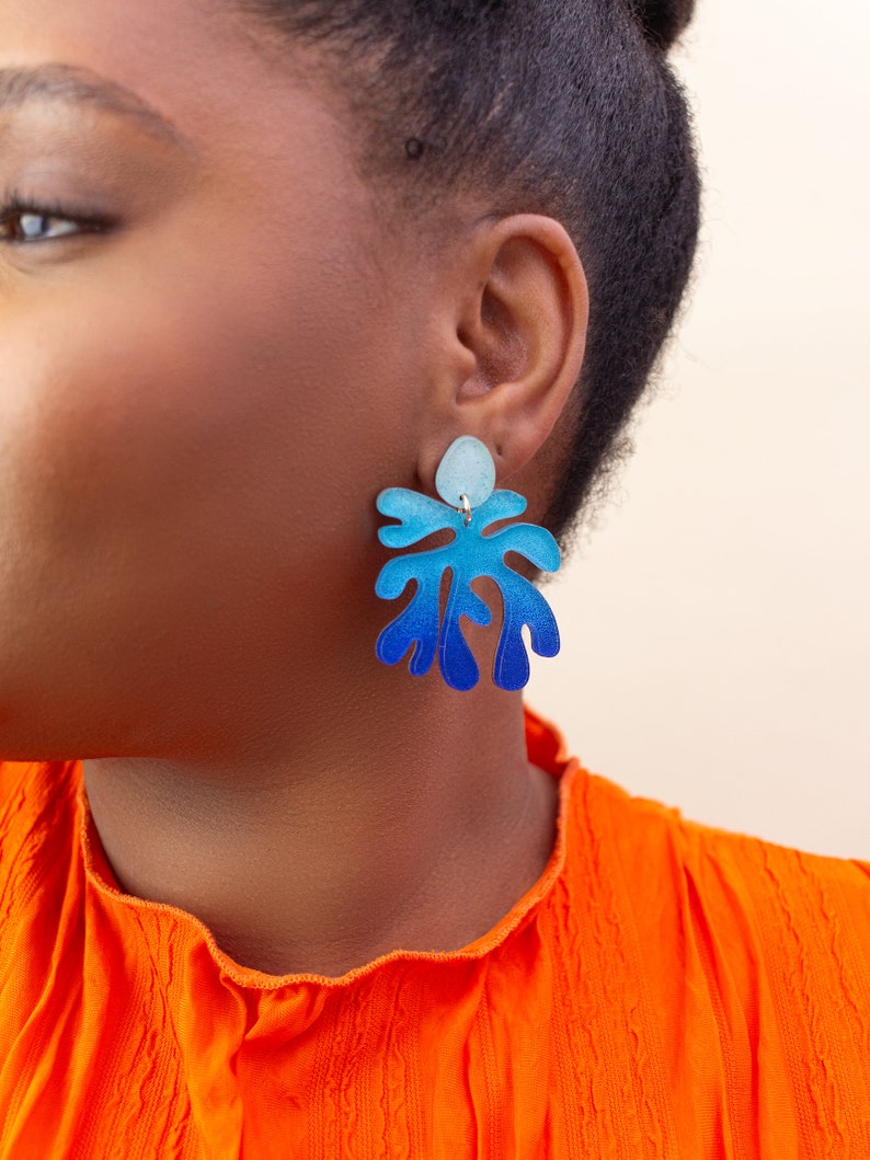 A close up of a model wearing A model wearing a pair of ombre blue Matisse inspired statement dangle earrings.