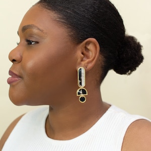 A model wearing a pair of black, white and gold acrylic statement earrings.