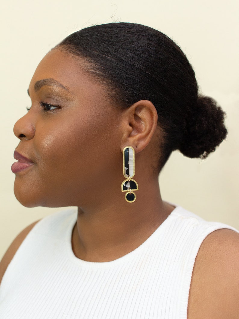 A model wearing a pair of black, white and gold acrylic statement earrings.