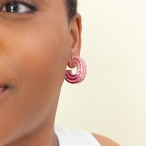 A model wearing a pair of pink acrylic statement hoop earrings.