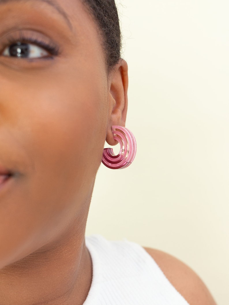 A model wearing a pair of pink acrylic statement hoop earrings.