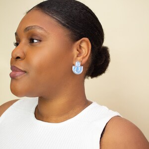 A model wearing blue statement stud earrings.