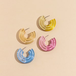 A group of midi-sized chunky acrylic statement hoop earrings in yellow, beige, pink, and blue.