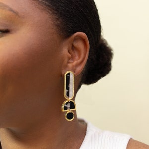 A model wearing a pair of black, white and gold acrylic statement earrings.