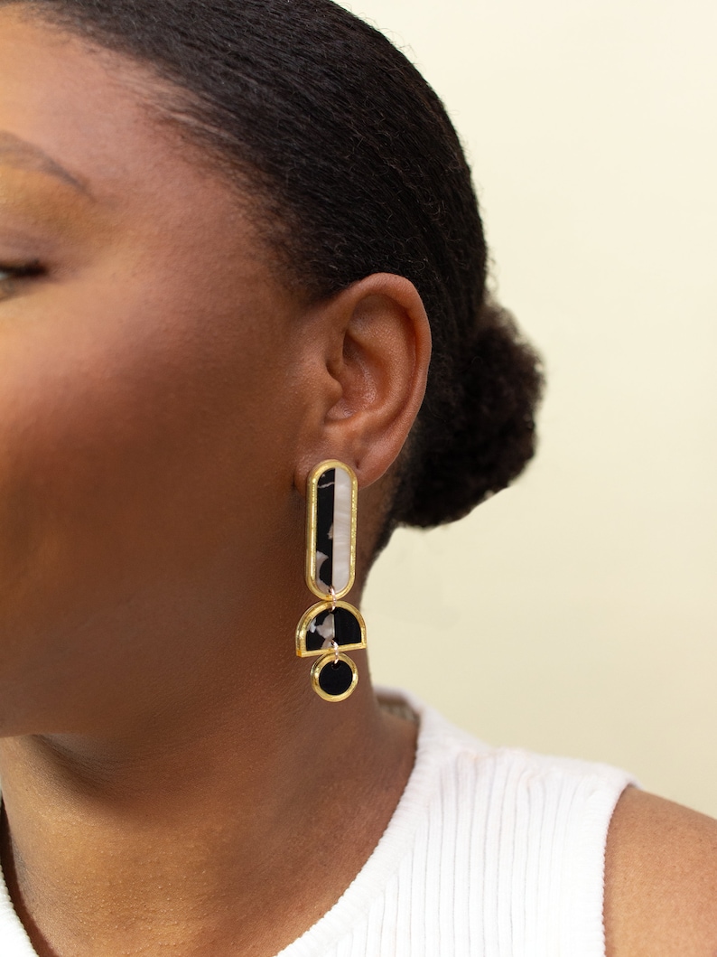 A model wearing a pair of black, white and gold acrylic statement earrings.