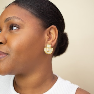 A close up of a model wearing a pair of Mother of Pearl and acrylic statement stud earrings