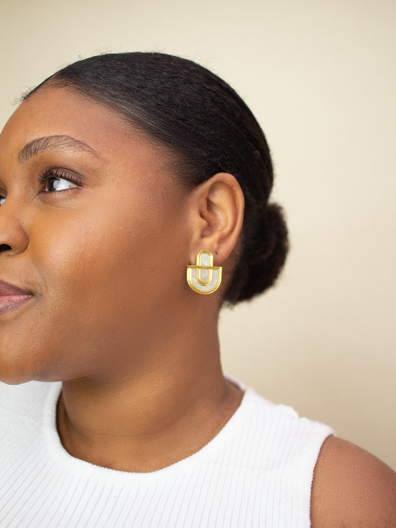 A close up of a model wearing a pair of Mother of Pearl and acrylic statement stud earrings