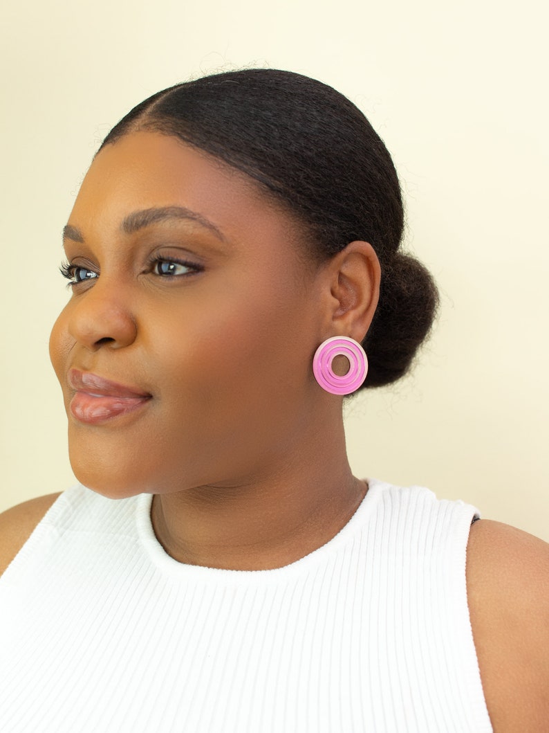 A model wearing  pink circular multicolored statement stud earrings.