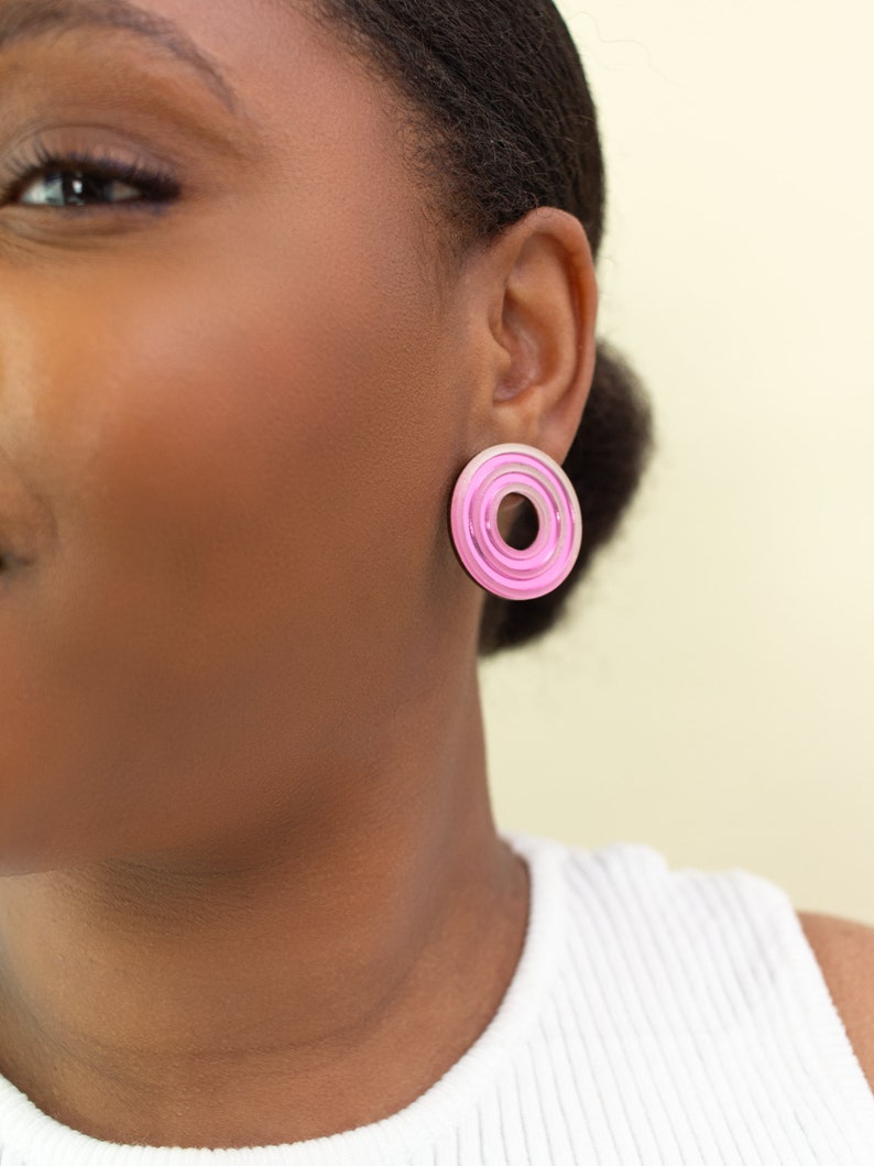 A close up of a model wearing  pink circular multicolored statement stud earrings.