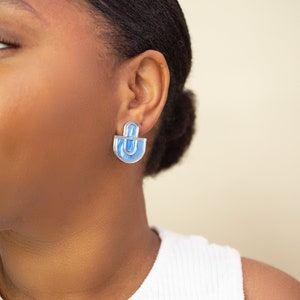 A model wearing blue and silver statement stud earrings.
