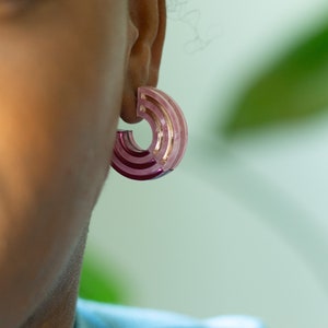 A close up of a model wearing a pair of pink acrylic statement hoop earrings.