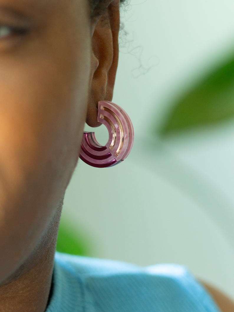 A close up of a model wearing a pair of pink acrylic statement hoop earrings.