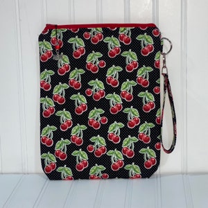 May include: A black zippered pouch with a red zipper and a black and white cherry print. The pouch has a black strap.