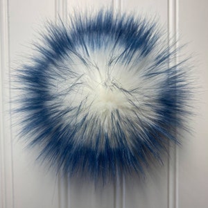 May include: A white faux fur pom pom with a blue trim around the edge.