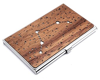 May include: A wooden business card holder with a silver metal frame. The wood has a dark brown color and a constellation design is cut out of the wood.