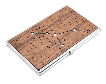 May include: A wooden business card holder with a silver metal frame. The wood has a dark brown color and features a constellation design with stars cut out.