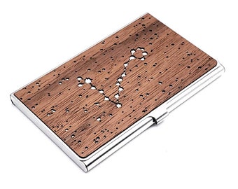May include: A brown wooden business card holder with a silver metal frame. The wood has a constellation design cut out of it.