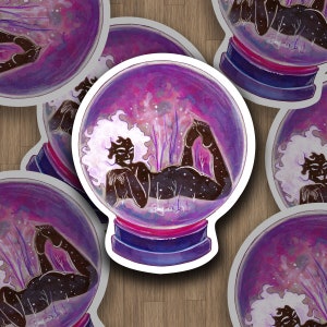 May include: A purple and white snow globe with a silhouette of a person with curly hair laying inside. The snow globe has a pink and purple base.