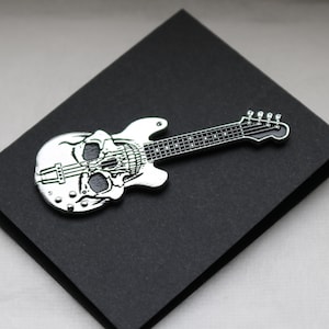 May include: A silver skull guitar pin with green details on a black background.